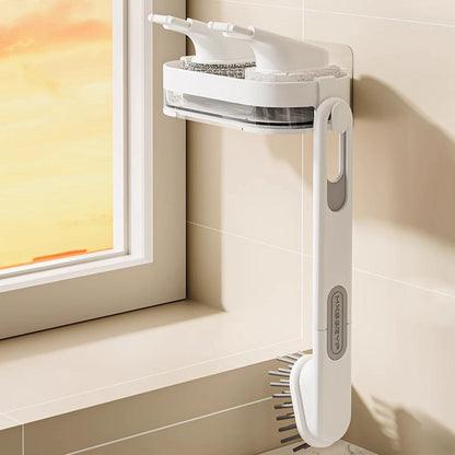 A white wall-mounted sink brush and sponge holder with a long handle brush hanging from it.