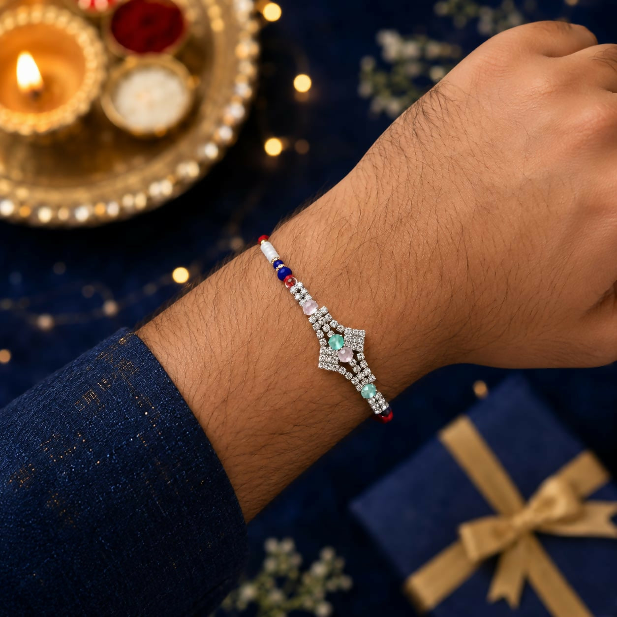 A man's arm wears a red thread bracelet with a silver-toned, crystal-studded centerpiece, against a blurred blue background