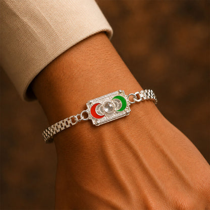 A person's arm wears a silver-colored bracelet with a rectangular centerpiece featuring red and green crescent moon shapes.