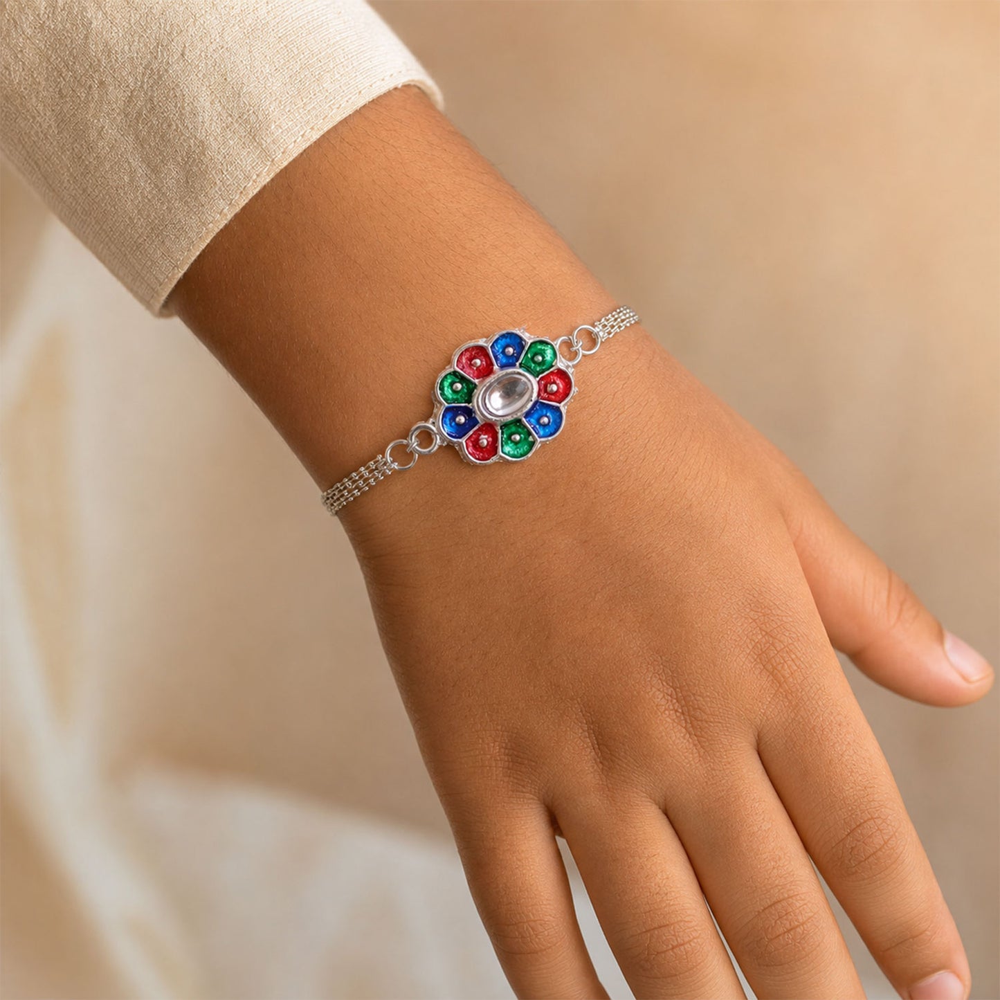 A person's wrist wears the silver chain bracelet with its colorful enamel flower charm, against a light-colored garment.