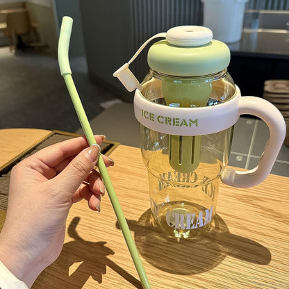 A hand holds a long green straw next to a clear bottle with a green lid and handle.