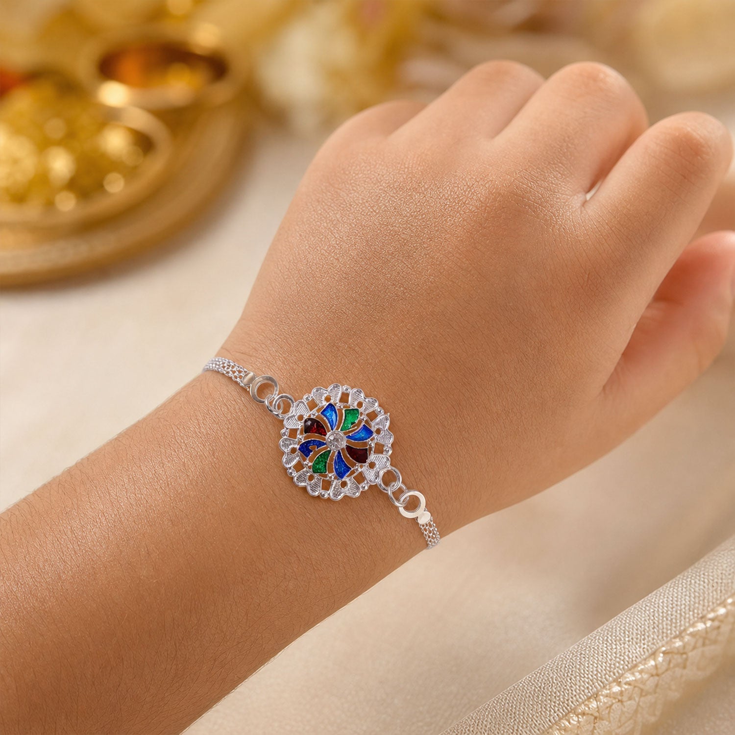 A person's wrist wears a silver chain bracelet with a round, colorful enamel and crystal centerpiece, against a soft,