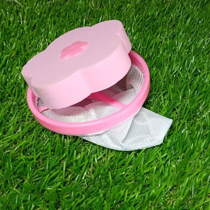 A pink flower-shaped lint filter with a white mesh bag rests on bright green artificial grass.