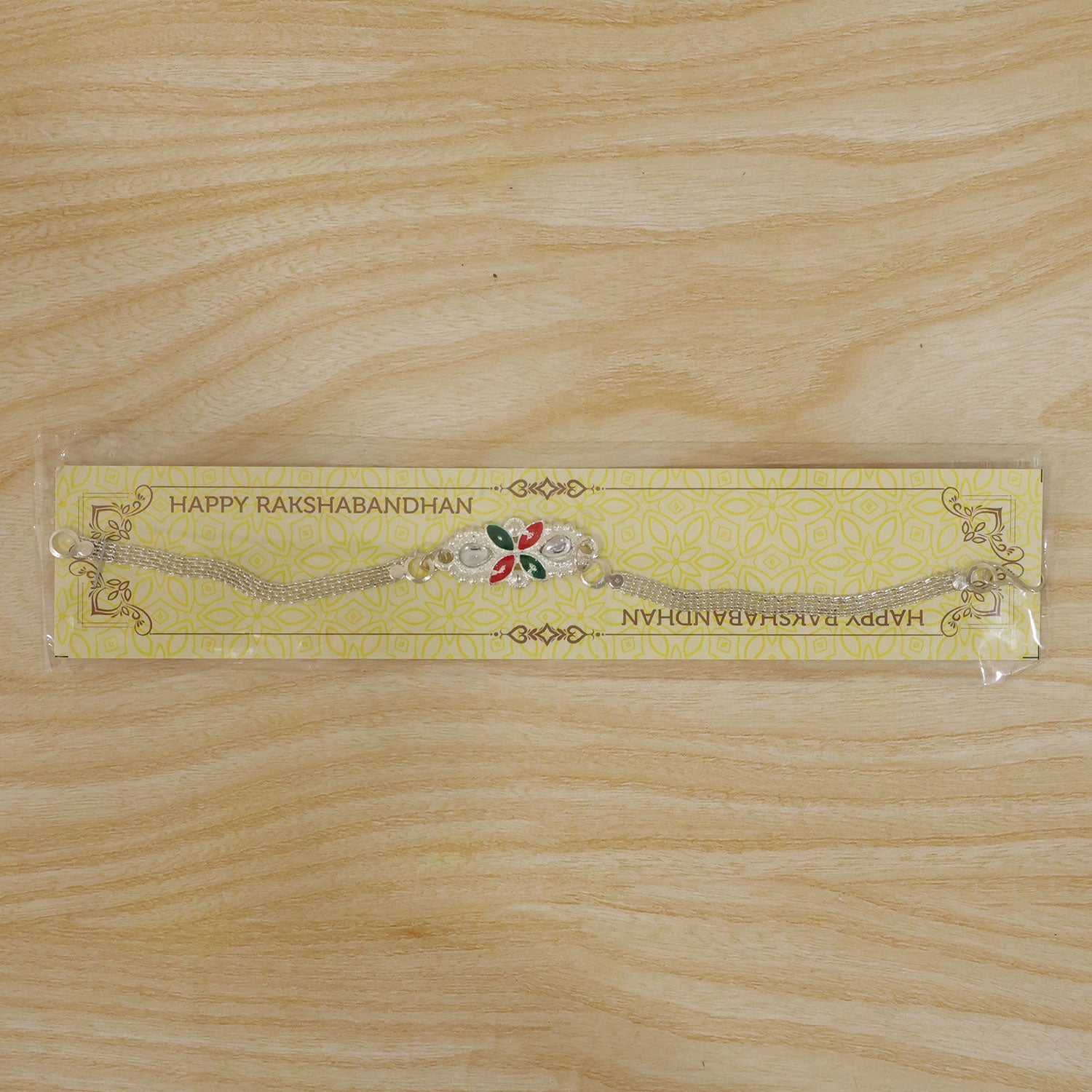 The silver-toned bracelet with its red and green enamel floral design is packaged on a yellow card with