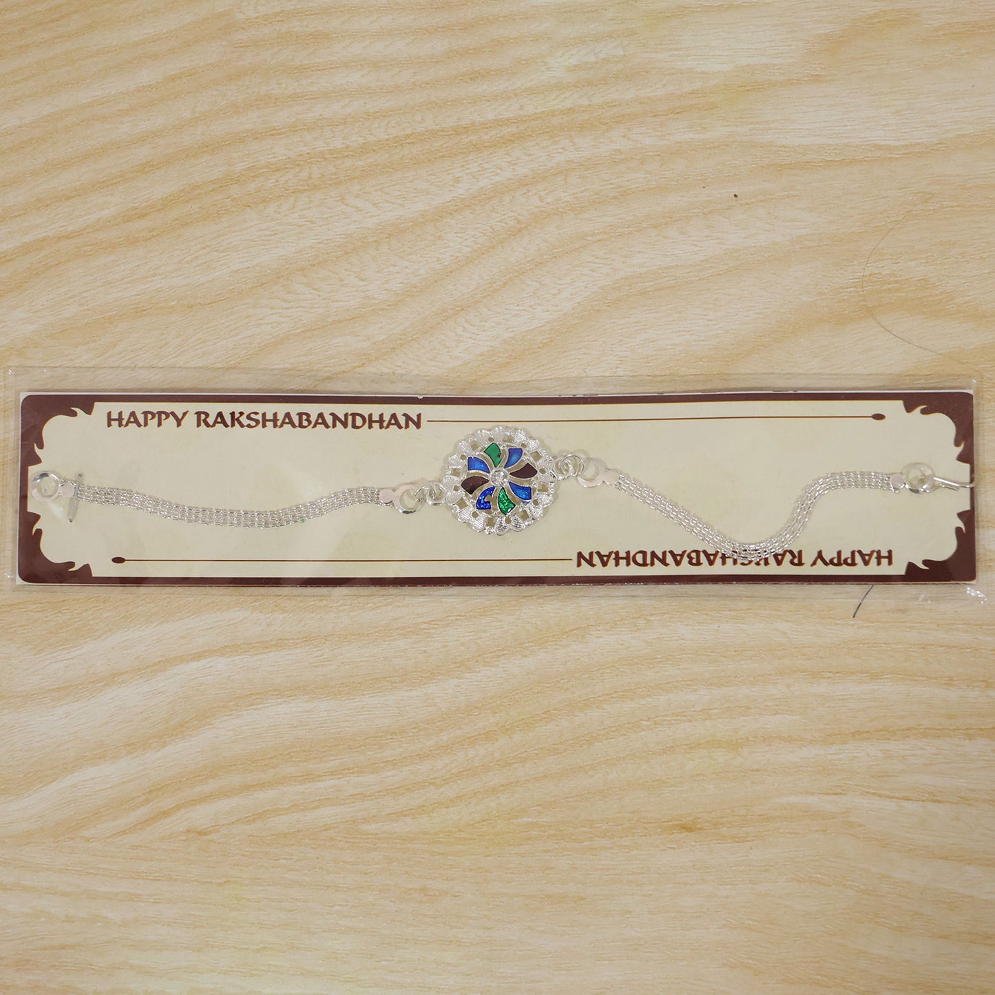 A silver chain bracelet with a round, colorful enamel and crystal centerpiece is packaged on a brown card with