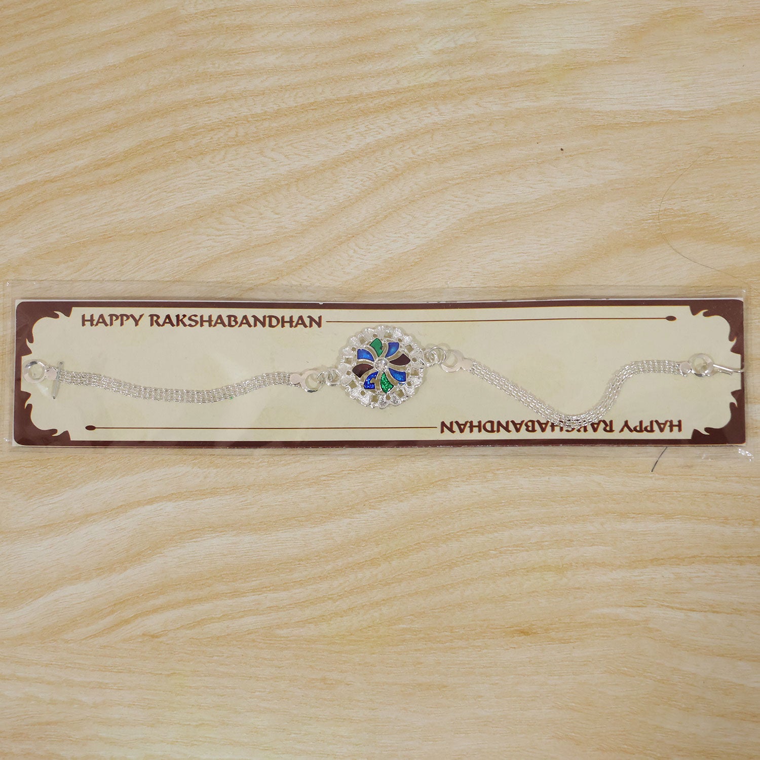 A silver chain bracelet with a round, colorful enamel and crystal centerpiece is packaged on a brown card with