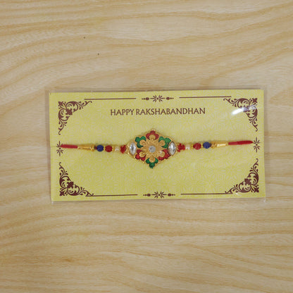 A gold-colored bracelet with a red, green, and white floral design, packaged on a yellow card, on a wooden surface.