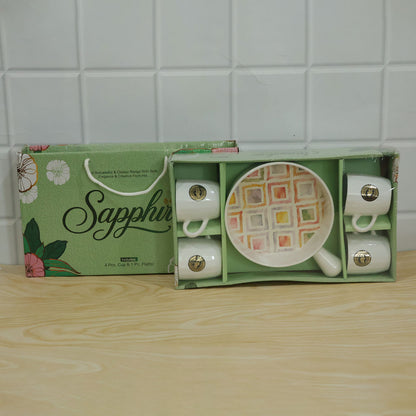 A green gift box containing a five-piece ceramic set, with four white mugs and a colorful patterned platter, sits on a