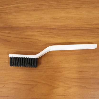 A white cleaning brush with black bristles rests on a warm brown wooden surface.
