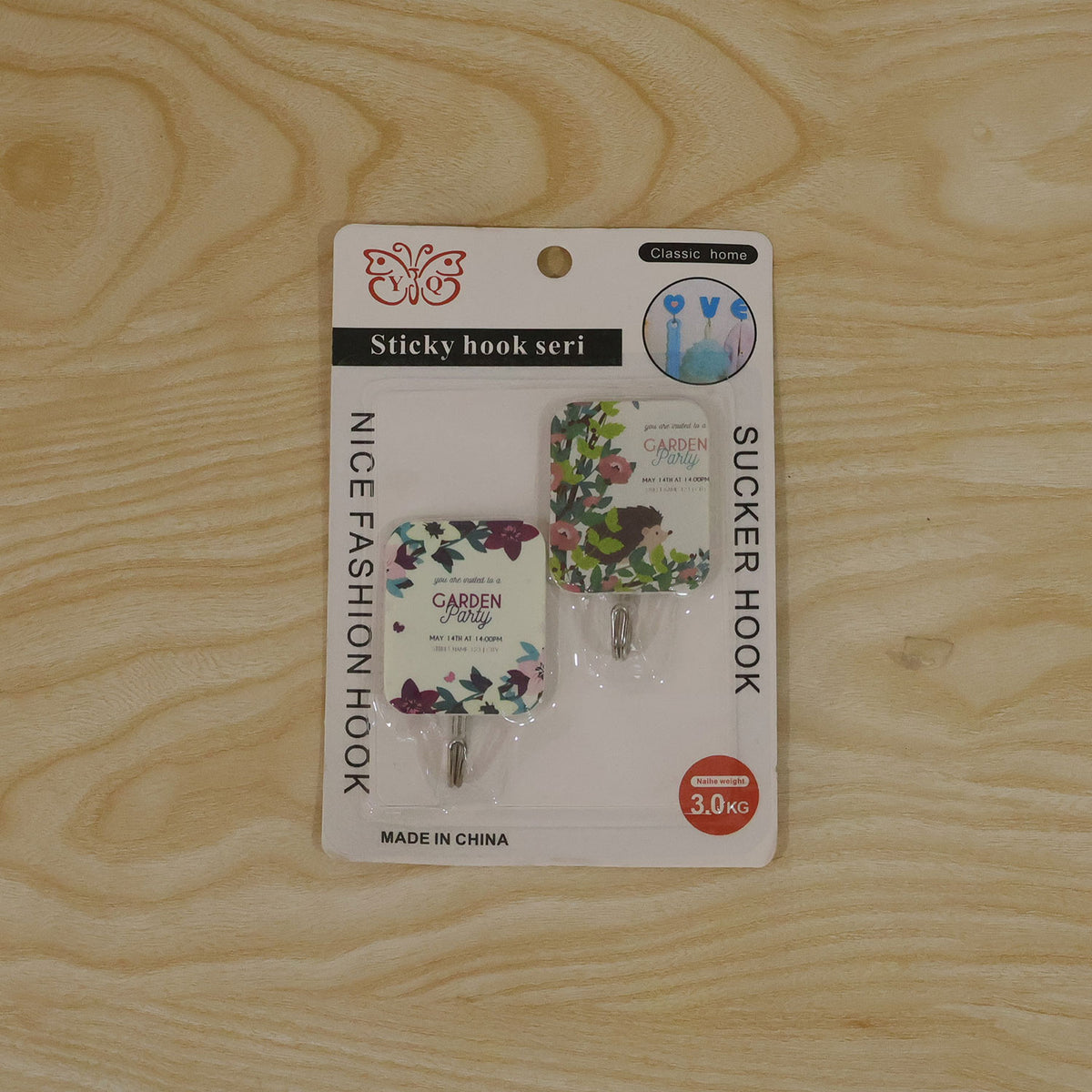 The two-piece set of floral sticky hooks in their retail packaging, lying flat on a light wooden surface.