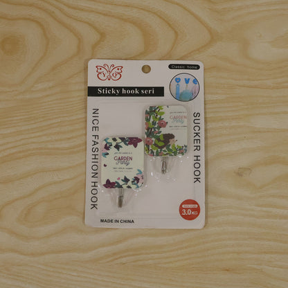 The two-piece set of floral sticky hooks in their retail packaging, lying flat on a light wooden surface.