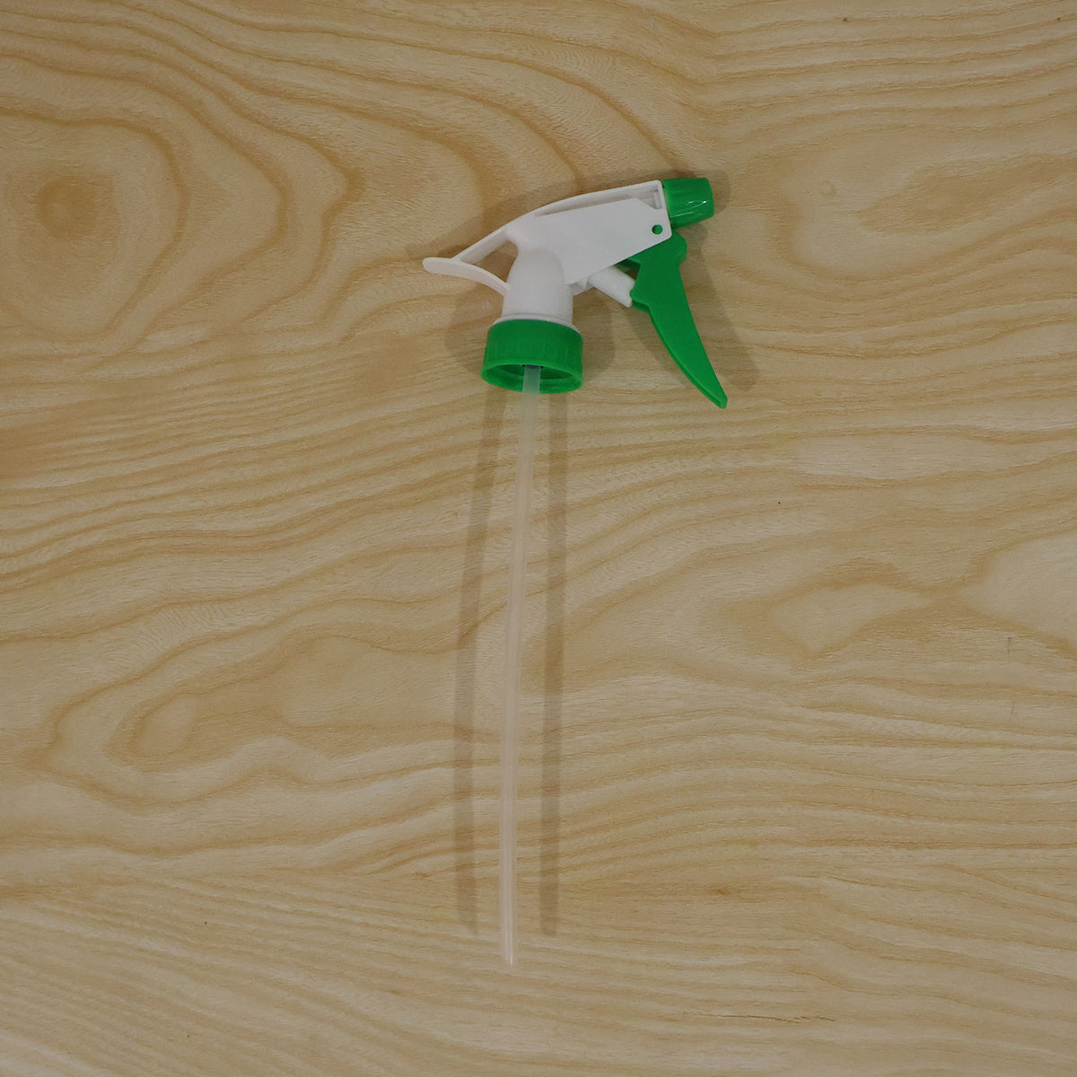 A white and green trigger sprayer nozzle with a long, clear dip tube resting on a light wood surface.