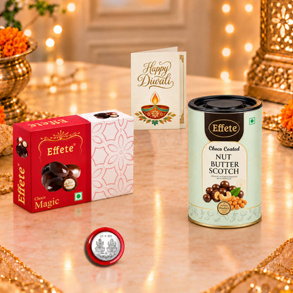Red chocolate box, nut butterscotch tin, silver coin, and greeting card on a marble table with blurred background.