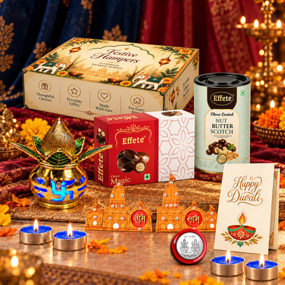 A Diwali gift set with a decorative box, sweets, a golden diya, and tealights, arranged on a red and gold patterned cloth.