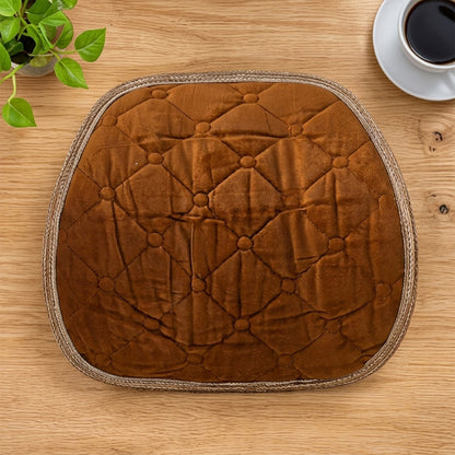 Overhead view of a brown quilted velvet cushion on a wooden desk with a plant and coffee.