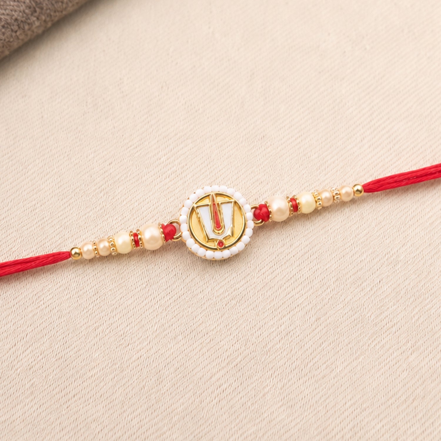 A close-up of the red and gold devotional thread, featuring a circular charm with a white beaded border and a gold U-shaped
