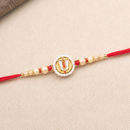 The devotional bracelet with a red string and a central gold Namam charm, surrounded by small white and gold beads, rests on