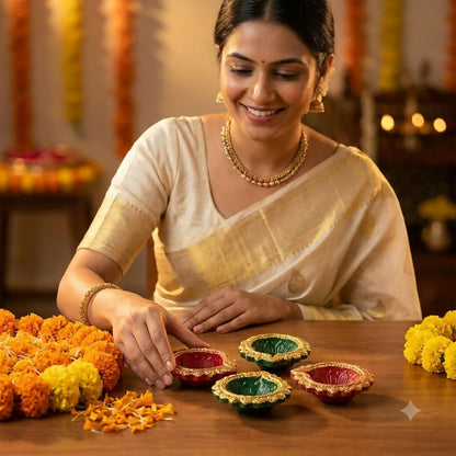 A woman in a cream saree arranges red and green diyas on a wooden table with marigold flowers.