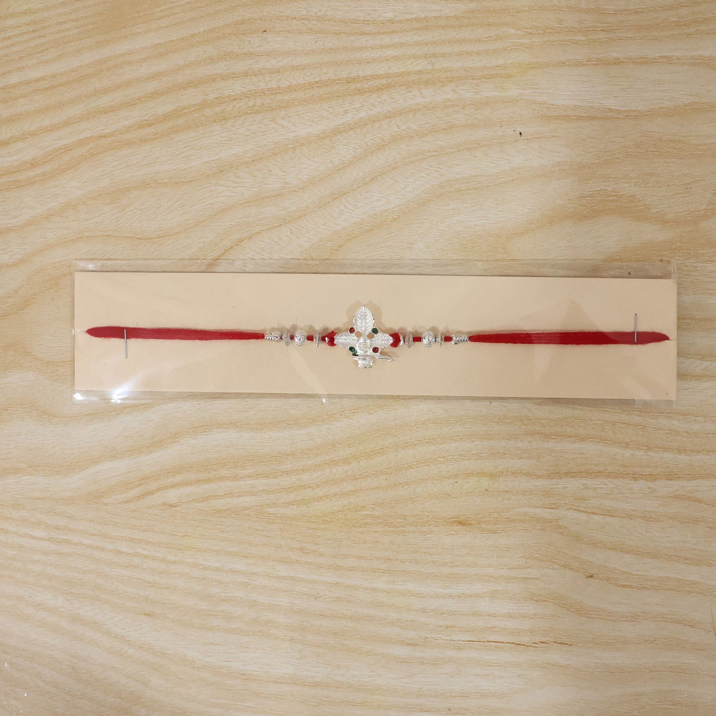 Silver Shivling Leaf Rakhi with Green Stones and Bright Red Thread
