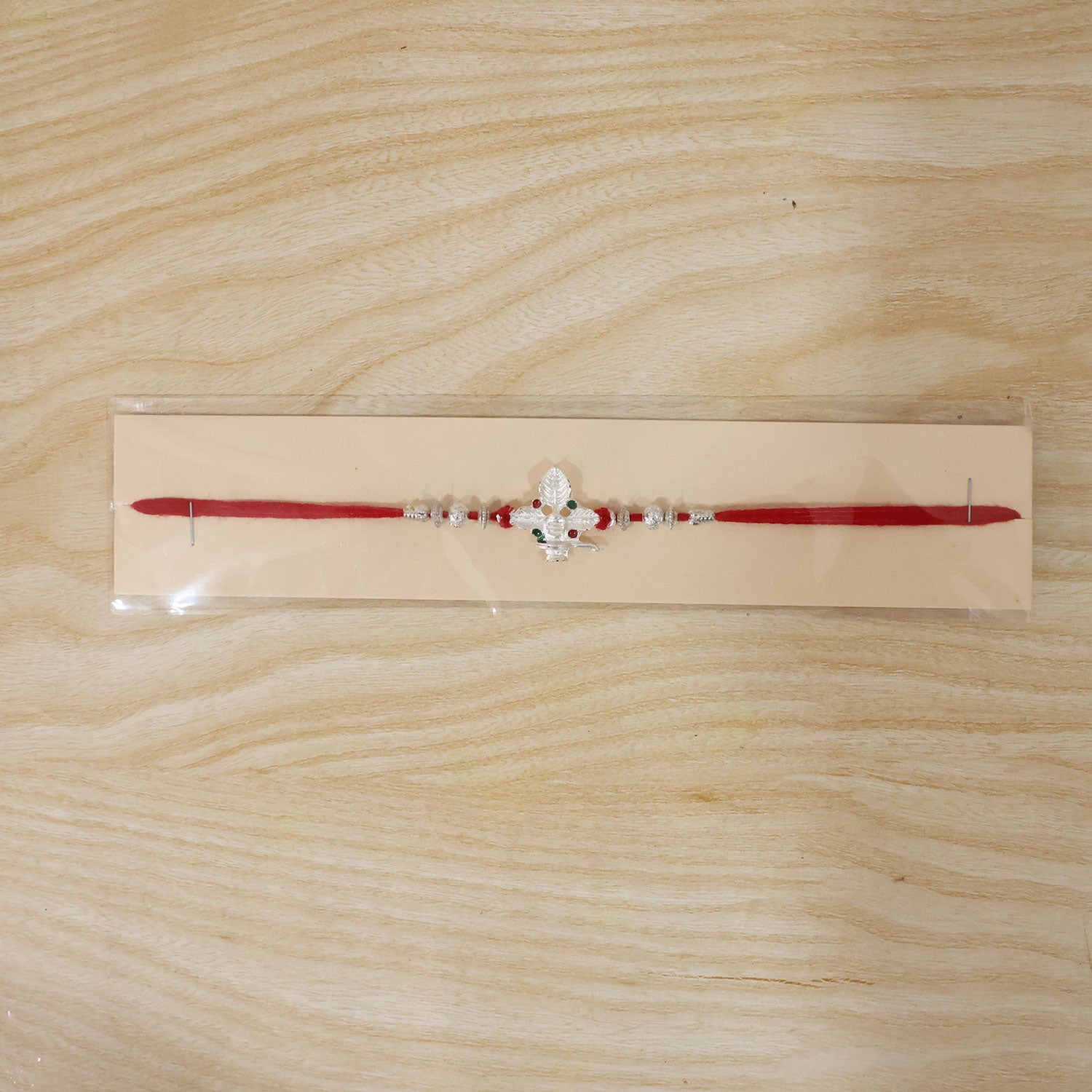 Silver Shivling Leaf Rakhi with Green Stones and Bright Red Thread