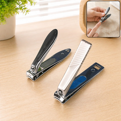Two stainless steel nail clippers, one dark grey and one silver, on a wooden table with a plant.