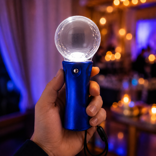Hand holding a blue disco ball light wand, illuminated with a white light, in a dimly lit room with bokeh lights.
