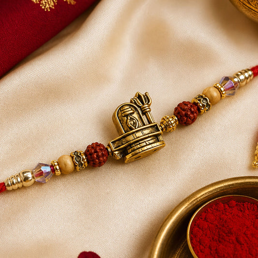 A red thread bracelet with a central antique gold Shivling and Trishul charm, flanked by red and gold beads, rests on a