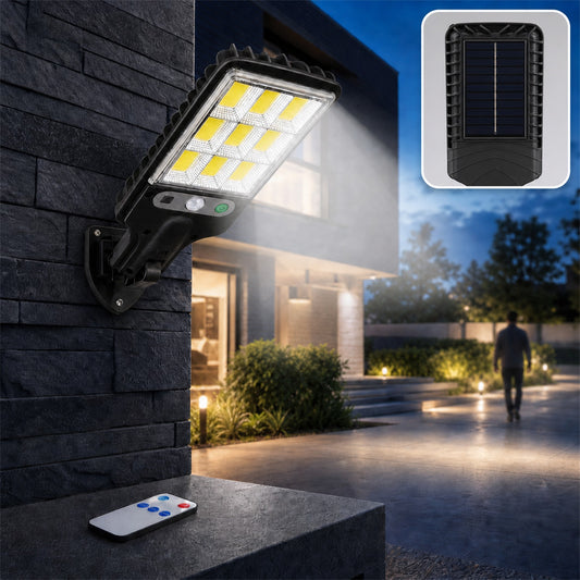 A black solar LED street light illuminates a modern house exterior and walkway at night, with a remote control on a ledge.