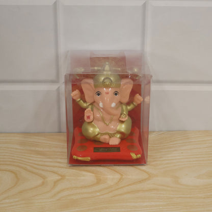 A peach and gold Ganesha idol on a red cushion with a solar panel, packaged in a clear plastic box.