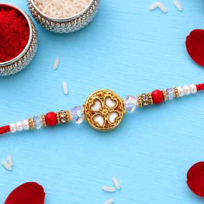 A red thread with a golden floral centerpiece and red, white, and clear beads, resting on a blue surface with rice grains