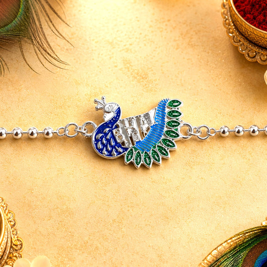 A silver peacock design with blue and green enamel sits on a beaded silver chain, with peacock feathers and red powder in
