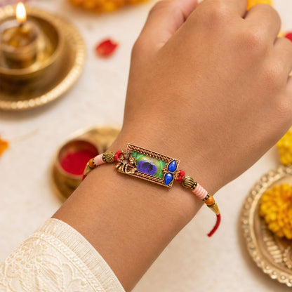 Close-up of the Radha Krishna motif and peacock feather detailing on the rakhi.