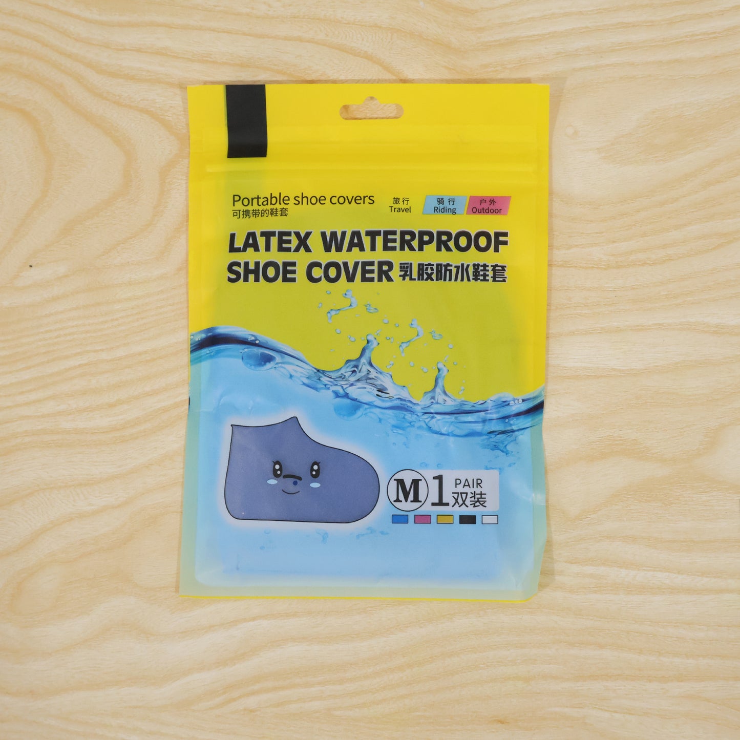 A yellow and clear plastic package for latex waterproof shoe covers, with text and a cartoon shoe, rests on a light wood