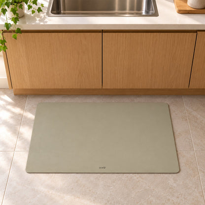 A light beige rectangular mat lies on tiled floor in a kitchen, beneath wooden cabinets and a sink.