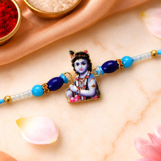 A blue and white beaded bracelet with a Lord Krishna charm is centered on a peach silk cloth, with rice and red powder in