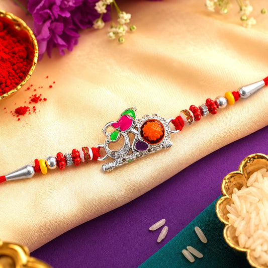 A red thread bracelet with a silver Om charm, adorned with colorful beads and an orange central gem, rests on a gold and