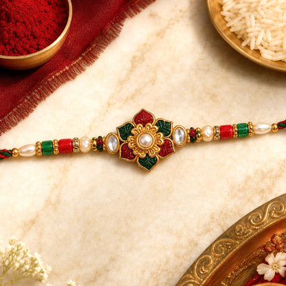 A red, green, and gold Meenakari Kundan bracelet with a central floral design, pearls, and red string, next to a bowl of red