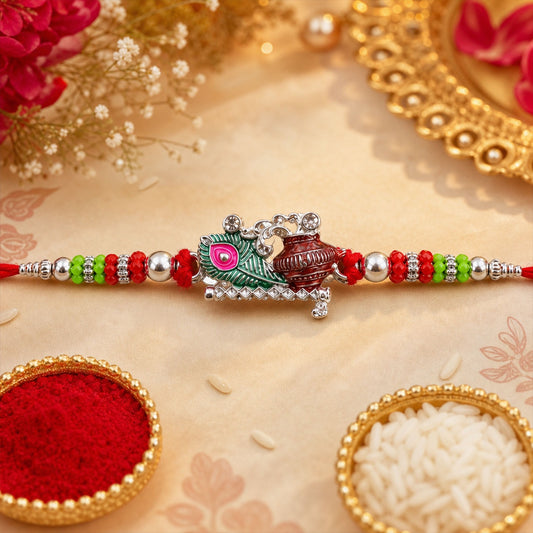 A vibrant Krishna Matki Rakhi with a silver Krishna and pot charm, flanked by red, green, and silver beads, rests on a beige