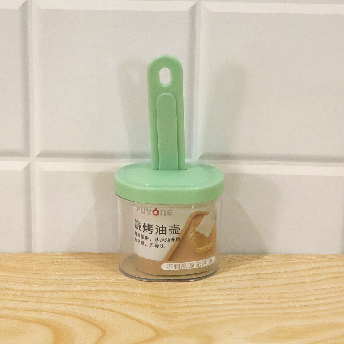 A light green silicone basting brush is stored in its clear container, which has a label with Chinese characters, on a
