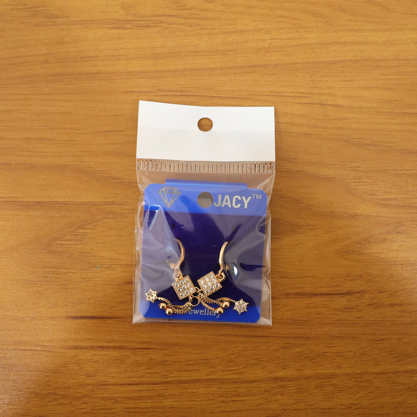 Pair of square drop earrings with sparkling stone cube and star charm in gold finish, worn on ear