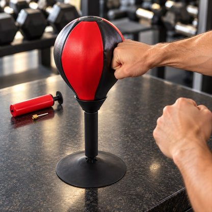 A person's hands near a red and black desktop punching ball, with one fist making contact.