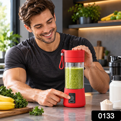 A man in a black t-shirt smiles while pressing the power button on a red portable blender with a green drink inside.