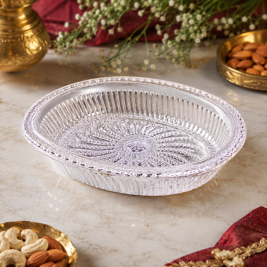 A silver oval decorative serving tray with a floral pattern on a marble surface with nuts and flowers.