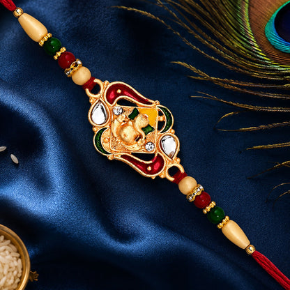 A gold-toned Ganesha charm with red, green, and yellow enamel, flanked by white stones and red, green, and cream beads,