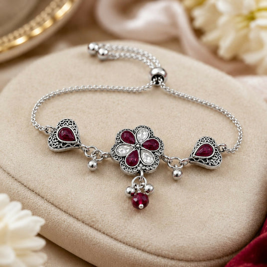 An antique silver adjustable slider bracelet with a central flower, two hearts, ruby-red pear stones, and dangling beads.