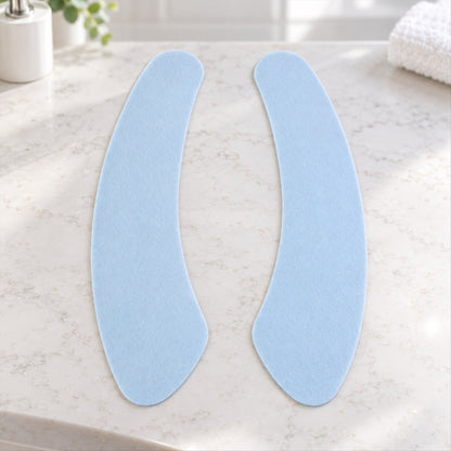 Two light blue, curved fabric pads are arranged on a white marble countertop in a bathroom.