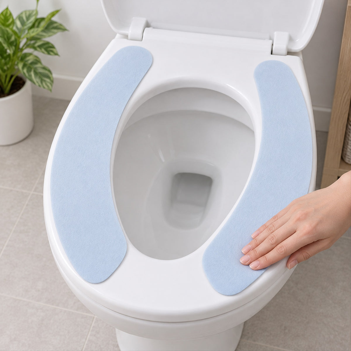 A hand adjusts a light blue fabric toilet seat pad on a white toilet, showing the soft texture.