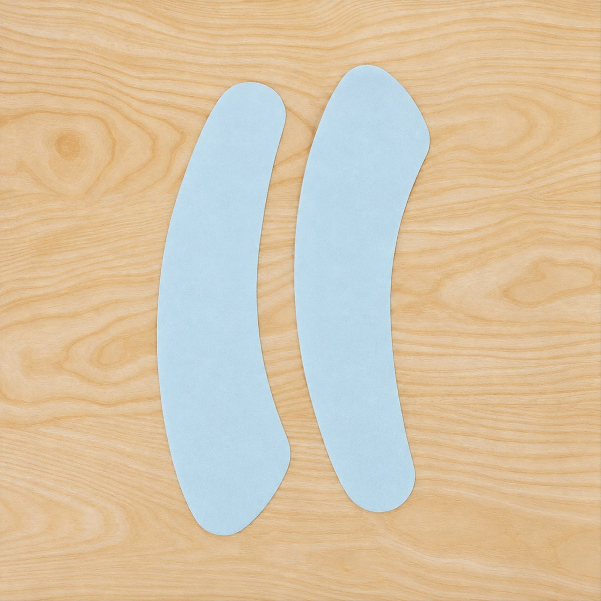 Two light blue, curved fabric pads are placed side by side on a light wooden surface.