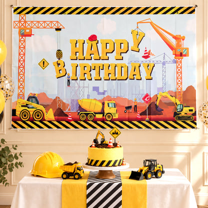 A construction-themed happy birthday banner hangs above a table with a cake, toy trucks, and a yellow hard hat.