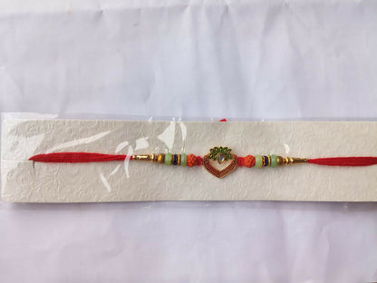 The red and gold bracelet with a heart charm and colorful beads is packaged in a clear plastic sleeve on a white textured